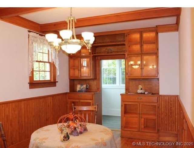 dining space featuring beamed ceiling, a chandelier, and wood walls