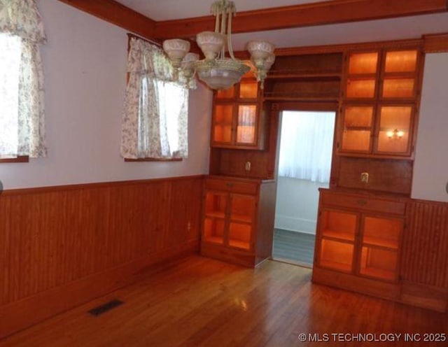 unfurnished dining area with hardwood / wood-style flooring, a chandelier, and wooden walls