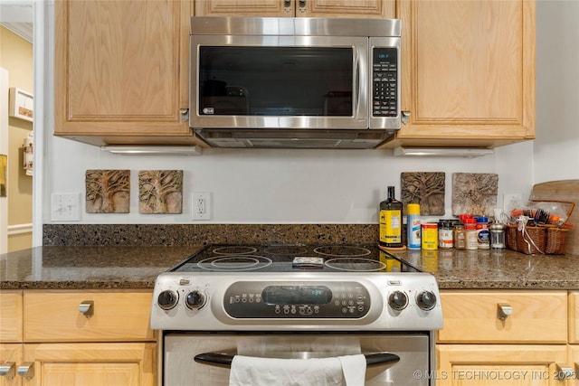 kitchen featuring stainless steel appliances, dark stone countertops, and light brown cabinetry