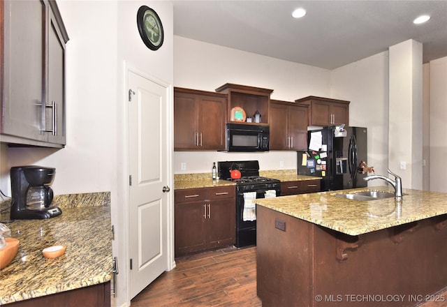 kitchen featuring dark brown cabinetry, a breakfast bar, sink, light stone counters, and black appliances