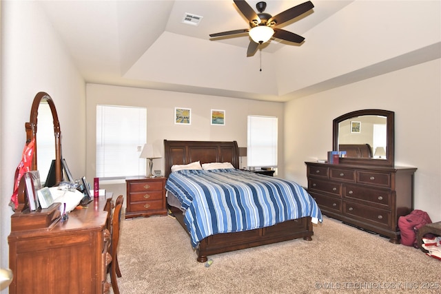 carpeted bedroom with a raised ceiling and ceiling fan