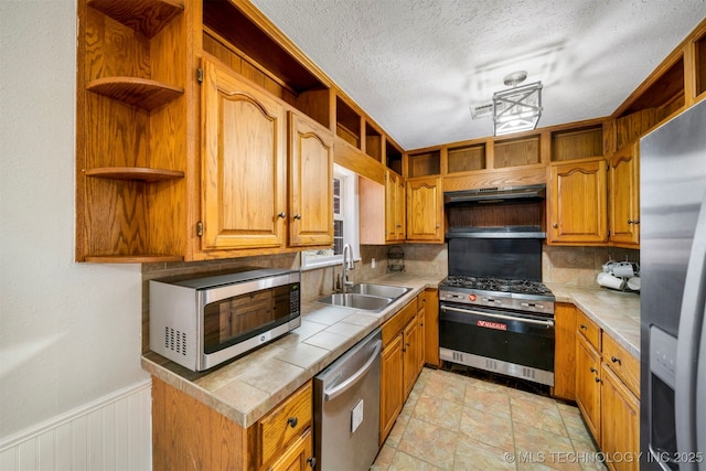 kitchen featuring sink, a textured ceiling, appliances with stainless steel finishes, tile counters, and backsplash