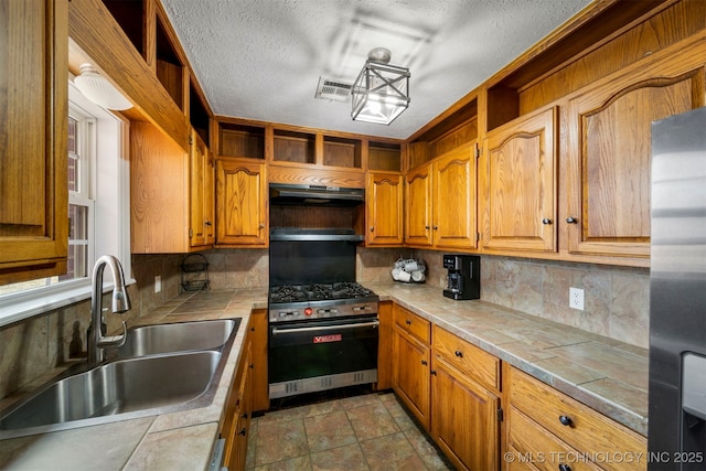 kitchen with a sink, open shelves, tile counters, appliances with stainless steel finishes, and under cabinet range hood