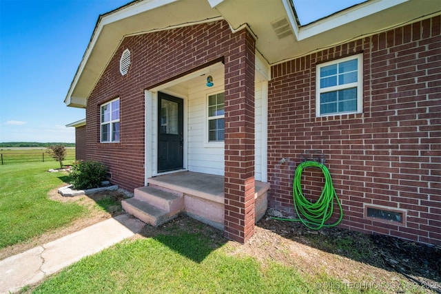 view of exterior entry featuring brick siding and a yard