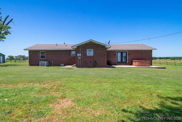 back of property with french doors, brick siding, a hot tub, and a lawn