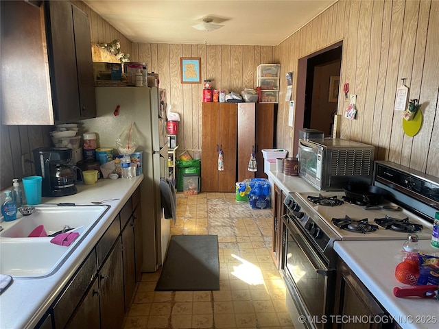 kitchen featuring sink, range with gas cooktop, wooden walls, and white fridge