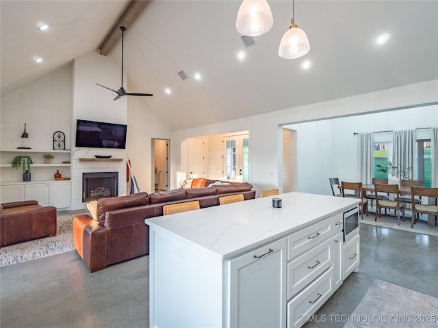 kitchen with white cabinetry, hanging light fixtures, a center island, light stone counters, and stainless steel microwave