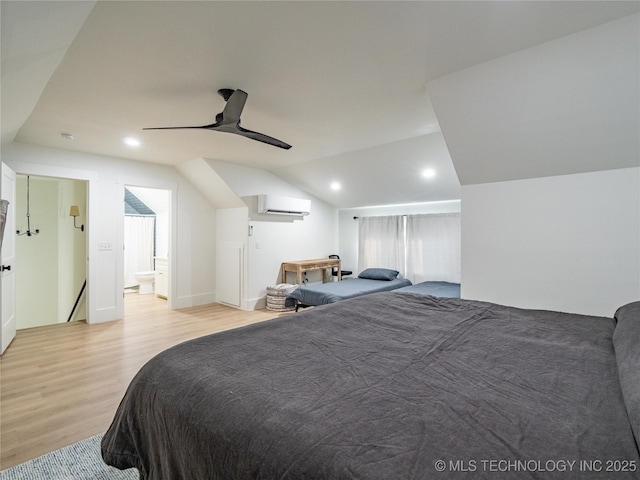 bedroom with ceiling fan, a wall mounted AC, ensuite bathroom, vaulted ceiling, and light wood-type flooring