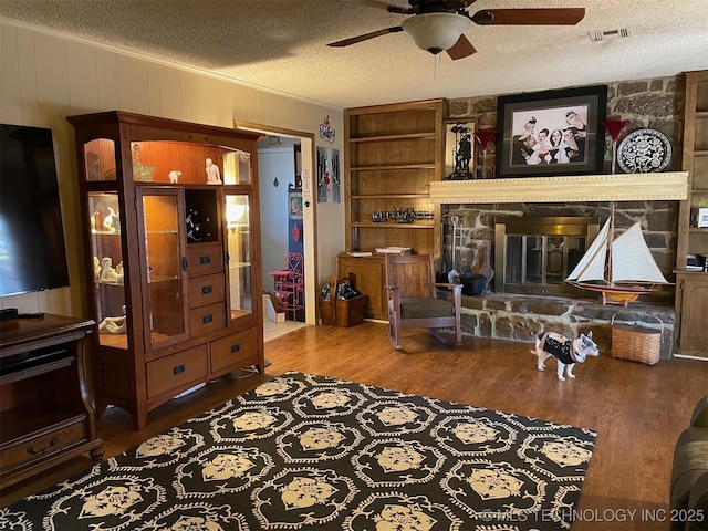 living room with ceiling fan, hardwood / wood-style floors, ornamental molding, a textured ceiling, and a stone fireplace