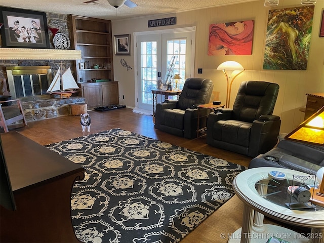 living room featuring ceiling fan, dark hardwood / wood-style floors, built in shelves, a textured ceiling, and a stone fireplace