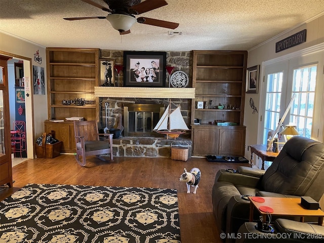 living room with wood-type flooring, a stone fireplace, ornamental molding, and a textured ceiling