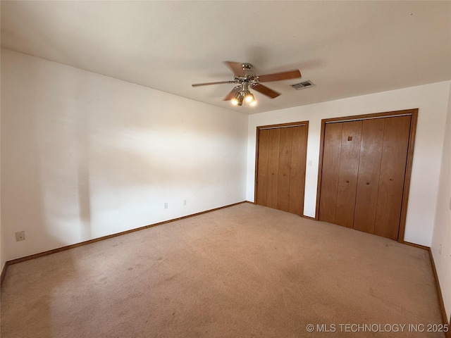 unfurnished bedroom with two closets, ceiling fan, and carpet flooring