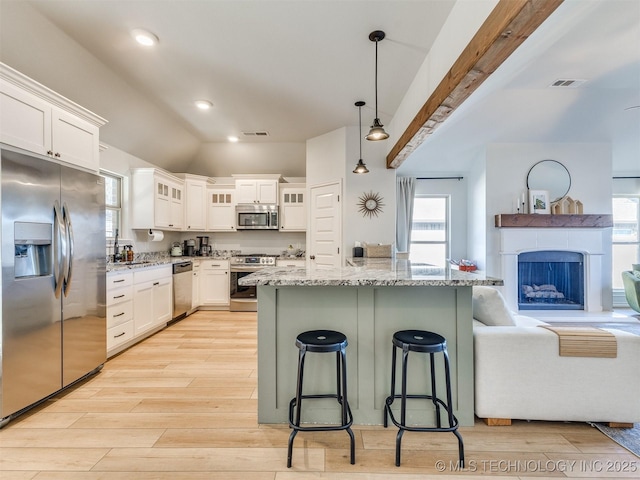 kitchen with a breakfast bar, white cabinetry, appliances with stainless steel finishes, pendant lighting, and light stone countertops