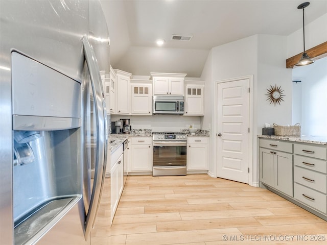 kitchen featuring vaulted ceiling, appliances with stainless steel finishes, pendant lighting, light stone countertops, and white cabinets