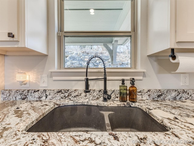 room details with light stone counters, sink, and white cabinetry