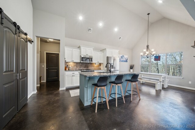 kitchen featuring pendant lighting, appliances with stainless steel finishes, a kitchen island with sink, white cabinets, and a barn door