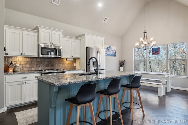 kitchen with decorative light fixtures, tasteful backsplash, white cabinets, stainless steel appliances, and a center island with sink