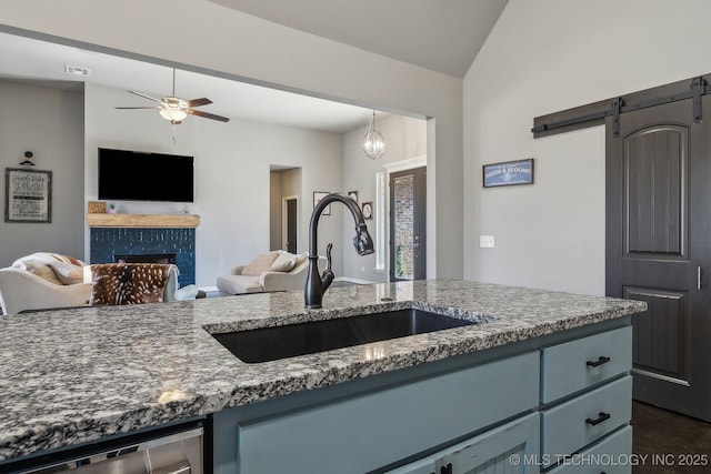 kitchen featuring sink, a tiled fireplace, vaulted ceiling, stainless steel dishwasher, and a barn door