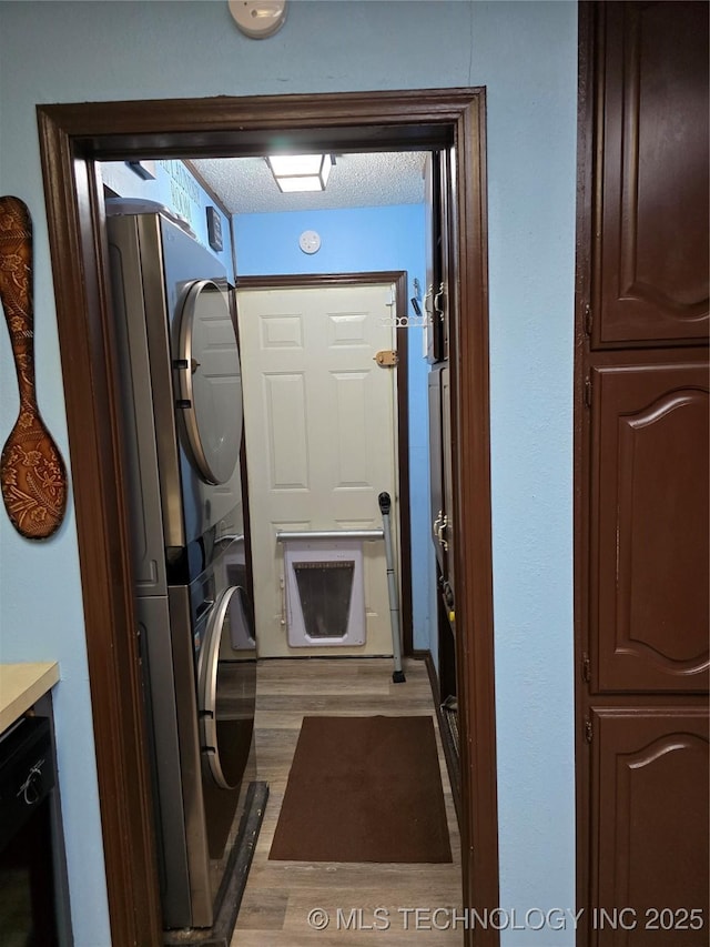 clothes washing area featuring stacked washer / drying machine, hardwood / wood-style floors, and a textured ceiling