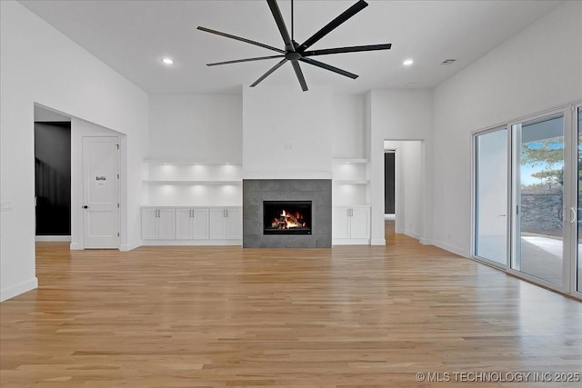 unfurnished living room with ceiling fan, a fireplace, and light wood-type flooring