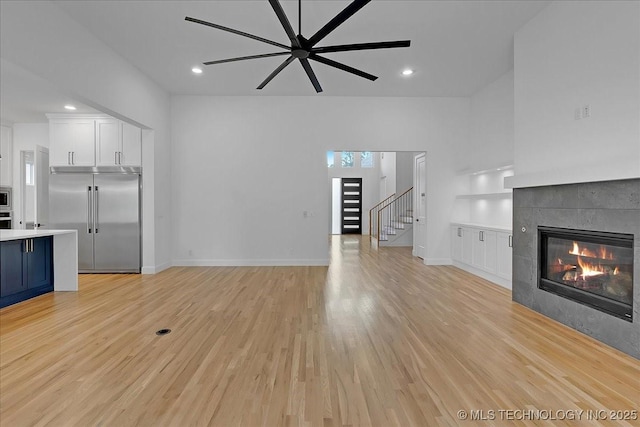 unfurnished living room featuring a tiled fireplace, light hardwood / wood-style flooring, and ceiling fan