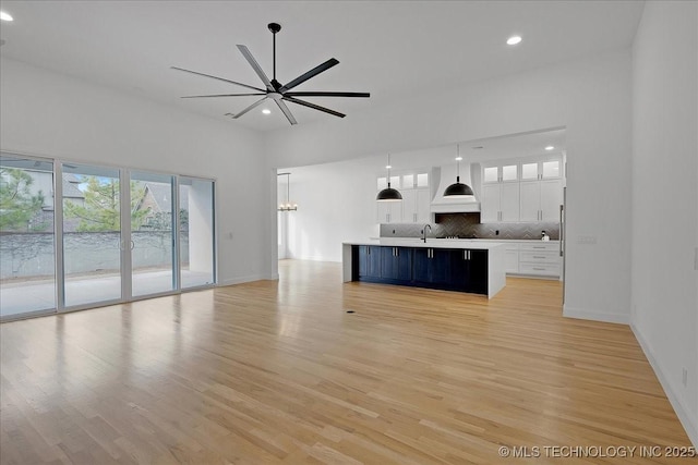 kitchen featuring custom exhaust hood, white cabinetry, an island with sink, pendant lighting, and backsplash