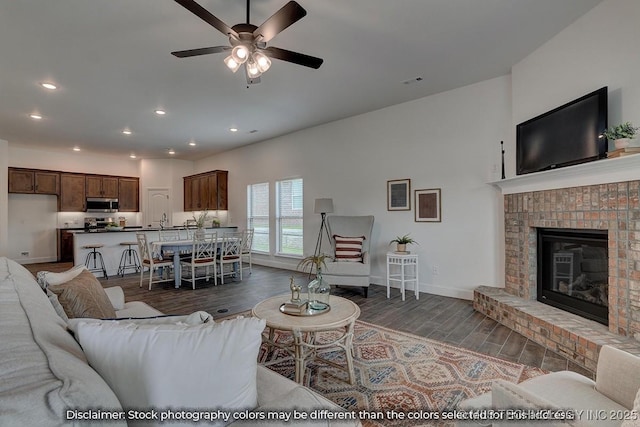 living room with a brick fireplace, dark hardwood / wood-style floors, sink, and ceiling fan