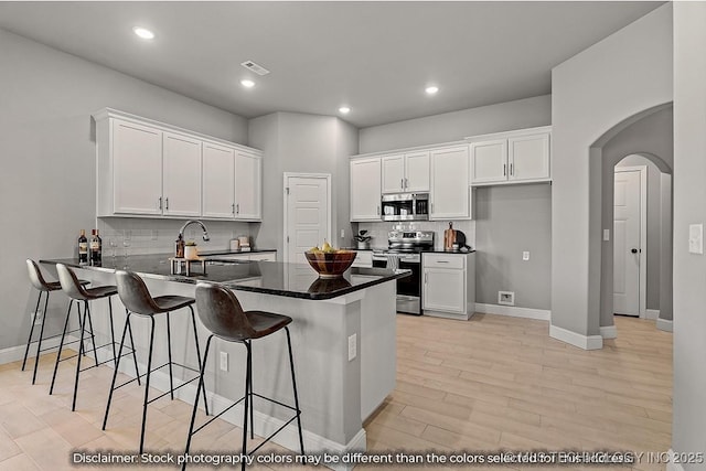 kitchen featuring appliances with stainless steel finishes, white cabinetry, a breakfast bar area, backsplash, and kitchen peninsula