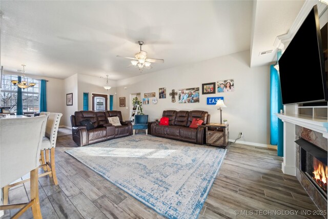 living room featuring hardwood / wood-style flooring, a tile fireplace, and ceiling fan with notable chandelier