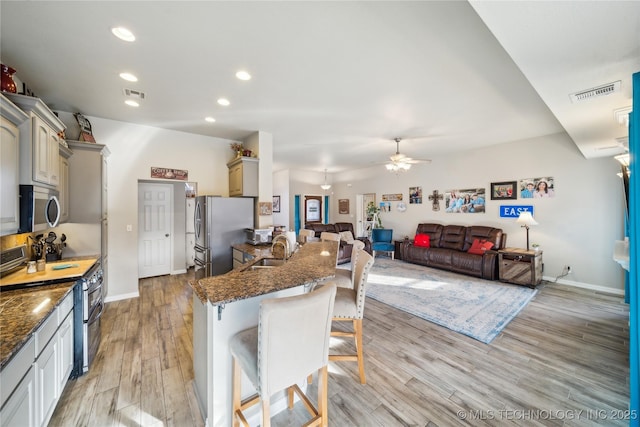 kitchen with sink, stainless steel appliances, light hardwood / wood-style floors, a kitchen bar, and dark stone counters