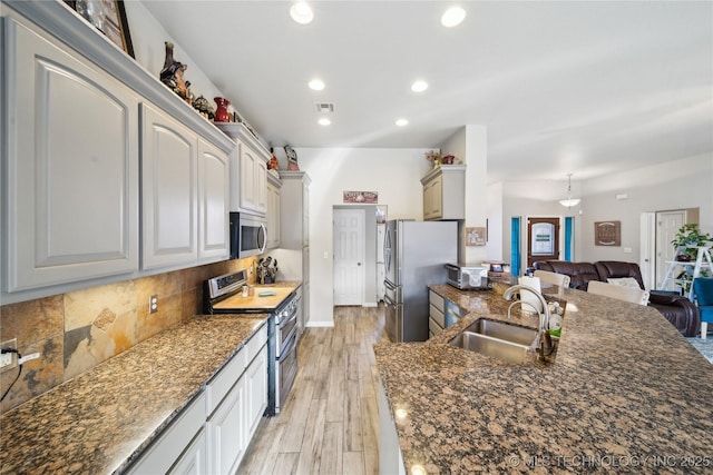 kitchen with sink, stainless steel appliances, tasteful backsplash, dark stone counters, and light wood-type flooring