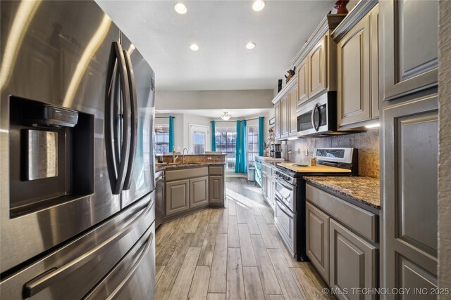 kitchen featuring appliances with stainless steel finishes, sink, dark stone countertops, backsplash, and light hardwood / wood-style floors