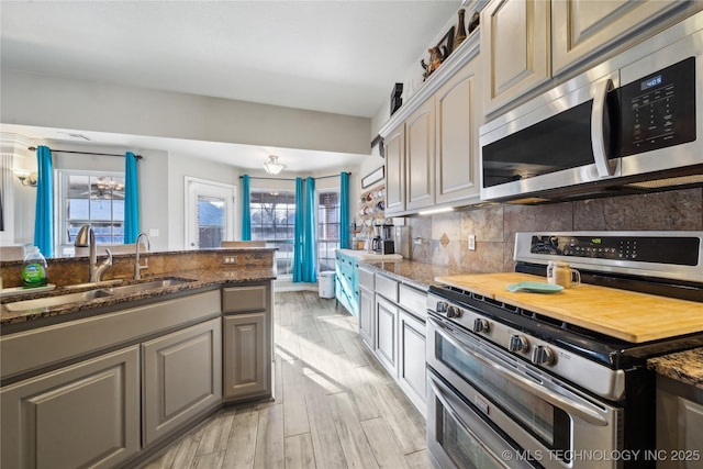 kitchen featuring sink, decorative backsplash, dark stone counters, light hardwood / wood-style floors, and stainless steel appliances