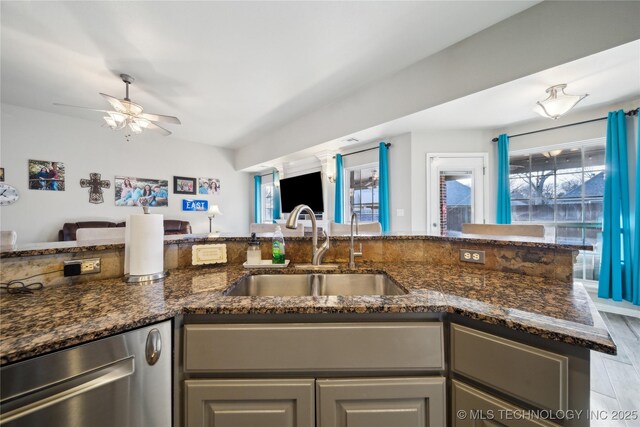 kitchen featuring dishwasher, sink, dark stone counters, ceiling fan, and light hardwood / wood-style flooring