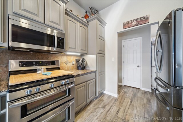 kitchen with gray cabinetry, light hardwood / wood-style flooring, stone counters, stainless steel appliances, and backsplash