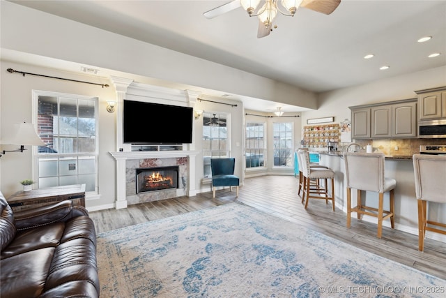 living room with ceiling fan, a high end fireplace, and light hardwood / wood-style floors