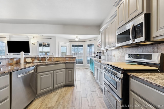 kitchen with sink, gray cabinetry, light stone counters, appliances with stainless steel finishes, and decorative backsplash