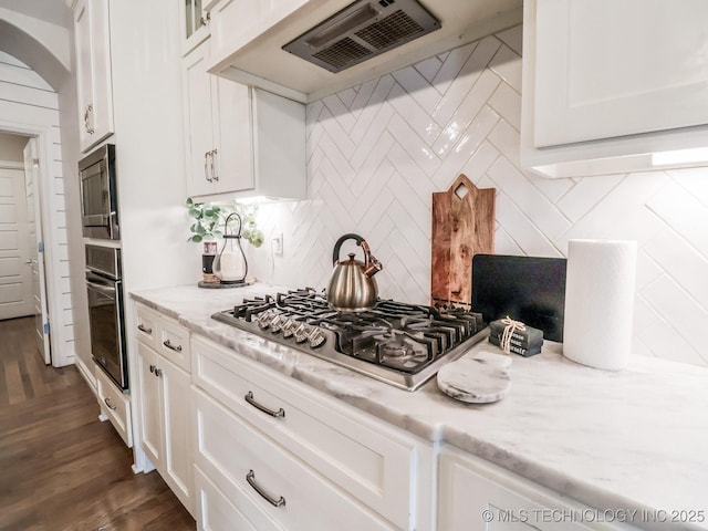 kitchen with premium range hood, appliances with stainless steel finishes, tasteful backsplash, light stone countertops, and white cabinets