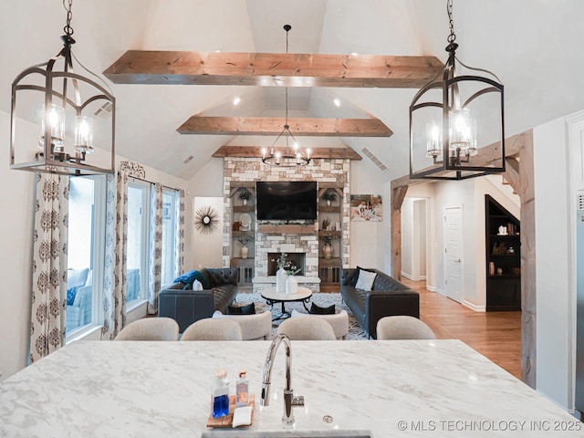 living room with an inviting chandelier, high vaulted ceiling, light hardwood / wood-style floors, a stone fireplace, and beamed ceiling