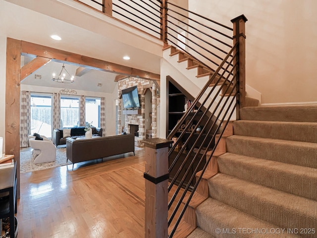 stairs with beamed ceiling, wood-type flooring, a fireplace, and a notable chandelier