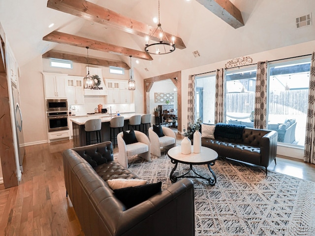 living room with beamed ceiling, a healthy amount of sunlight, hardwood / wood-style floors, and an inviting chandelier