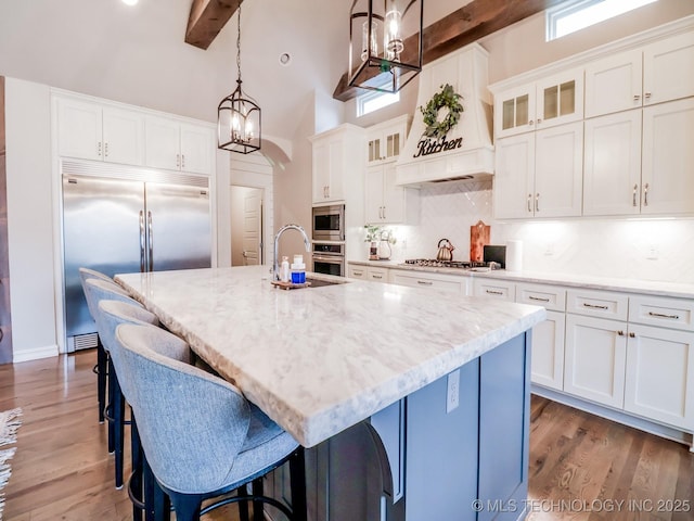 kitchen with built in appliances, decorative light fixtures, and a center island with sink