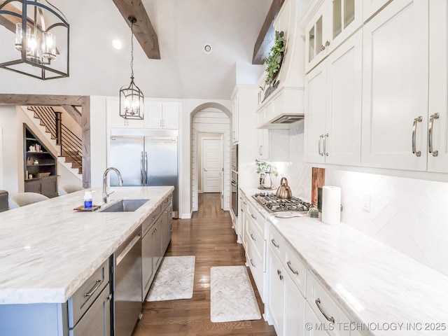 kitchen with appliances with stainless steel finishes, white cabinetry, hanging light fixtures, light stone counters, and an island with sink