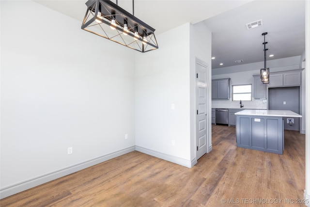 kitchen with gray cabinetry, decorative light fixtures, stainless steel dishwasher, a kitchen island, and hardwood / wood-style floors