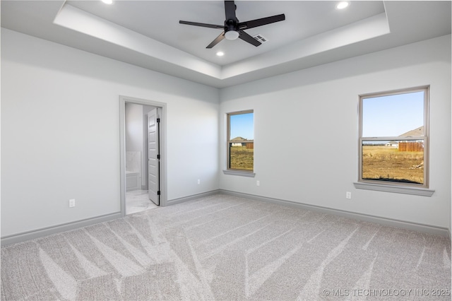 carpeted spare room with a raised ceiling and ceiling fan