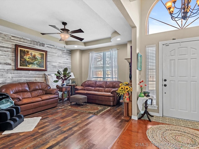 living room featuring hardwood / wood-style floors, ceiling fan with notable chandelier, a raised ceiling, and wood walls