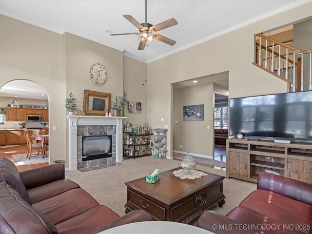 carpeted living room with a high ceiling, ceiling fan, ornamental molding, and a fireplace