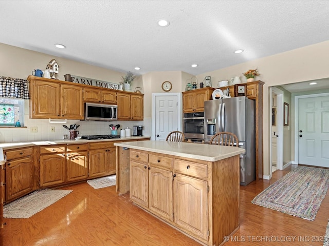 kitchen featuring light wood-type flooring, decorative backsplash, a center island, stainless steel appliances, and a textured ceiling