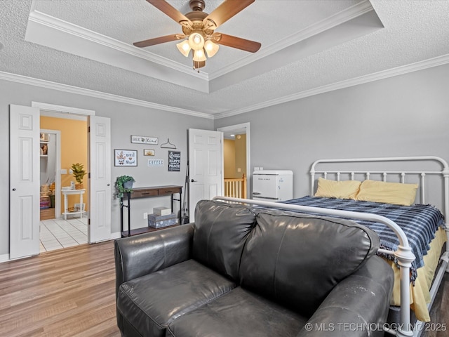 bedroom featuring a tray ceiling, crown molding, light hardwood / wood-style flooring, and ceiling fan