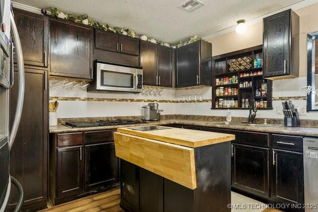 kitchen featuring butcher block counters, sink, a center island, dark brown cabinets, and appliances with stainless steel finishes